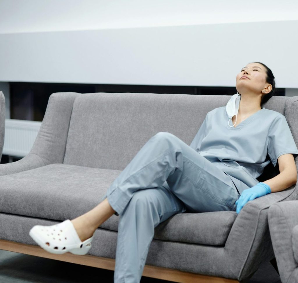 Nurse in scrubs takes a break, resting on a comfy hospital couch after a long shift.